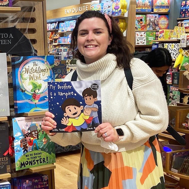 Kirstin McNeil in a bookshop holding a copy of My Brother is a Vampire